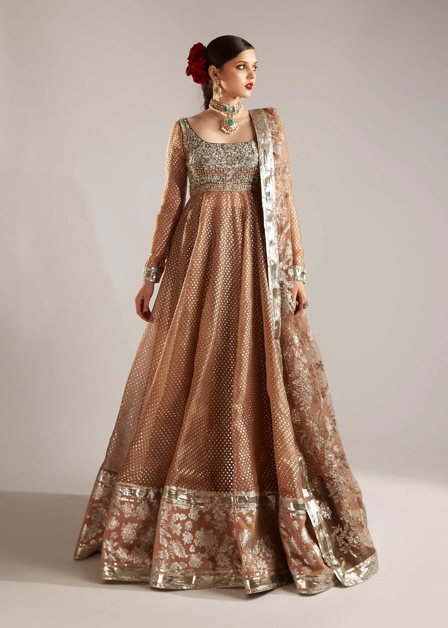 Woman wearing a traditional brown and gold embroidered outfit on a plain background