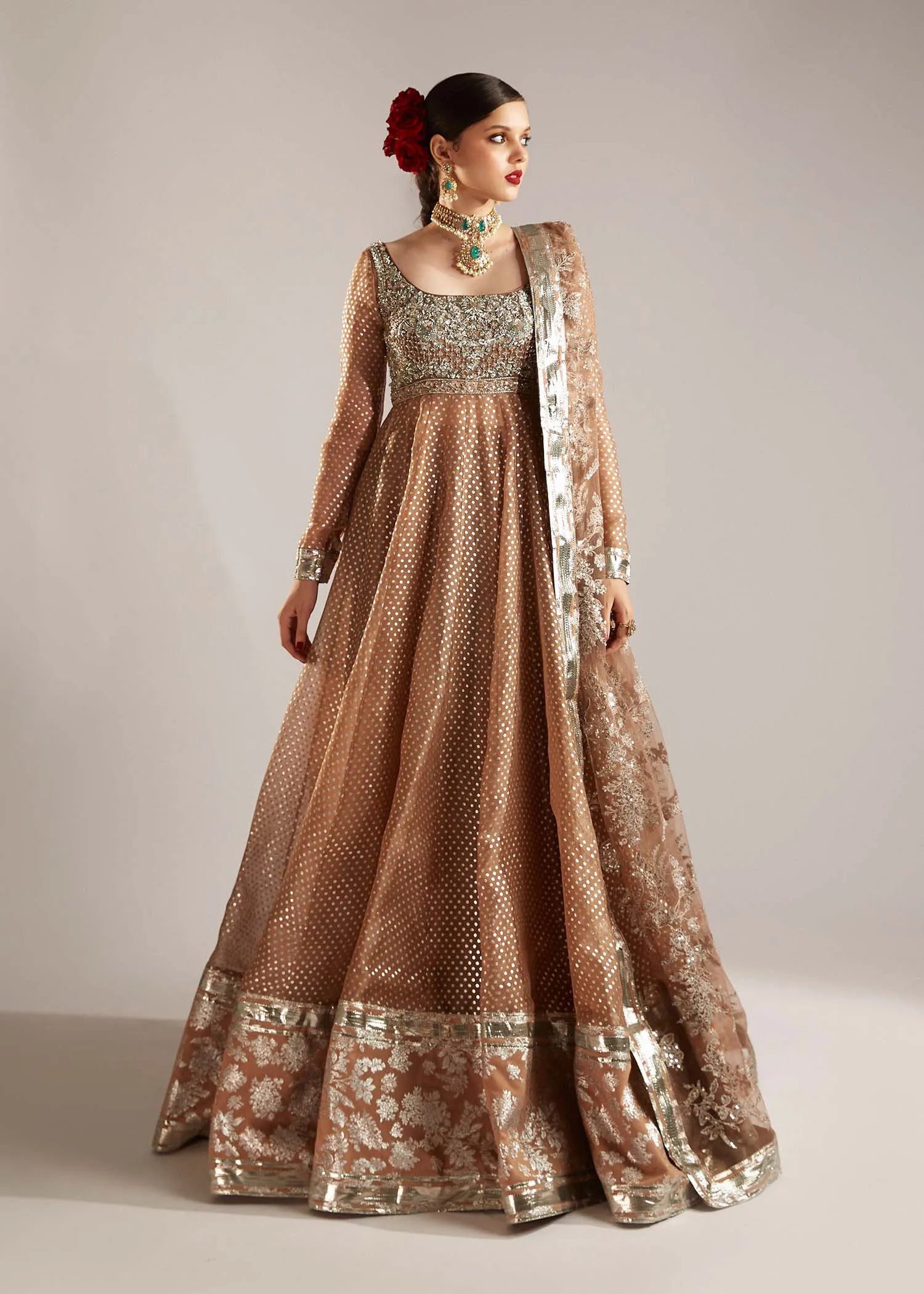 Woman wearing a traditional brown and gold embroidered outfit on a plain background