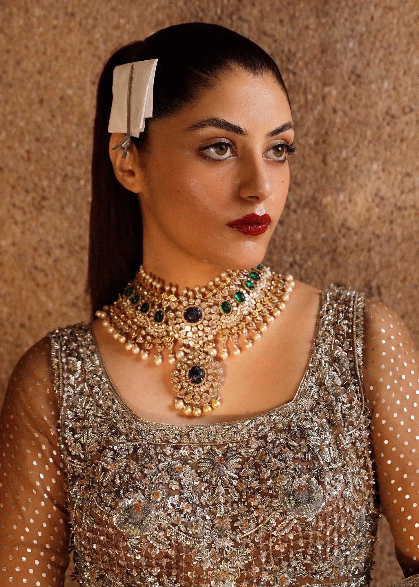Woman wearing a gold necklace with green gemstones against a textured brown background