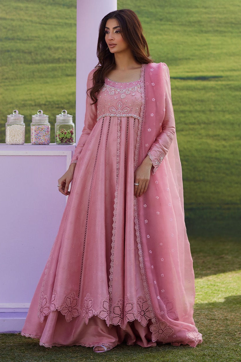 Woman in a pink traditional outfit standing outdoors with a green field background