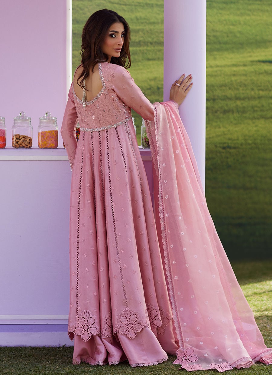 Woman in a pink traditional outfit standing outdoors with a green background