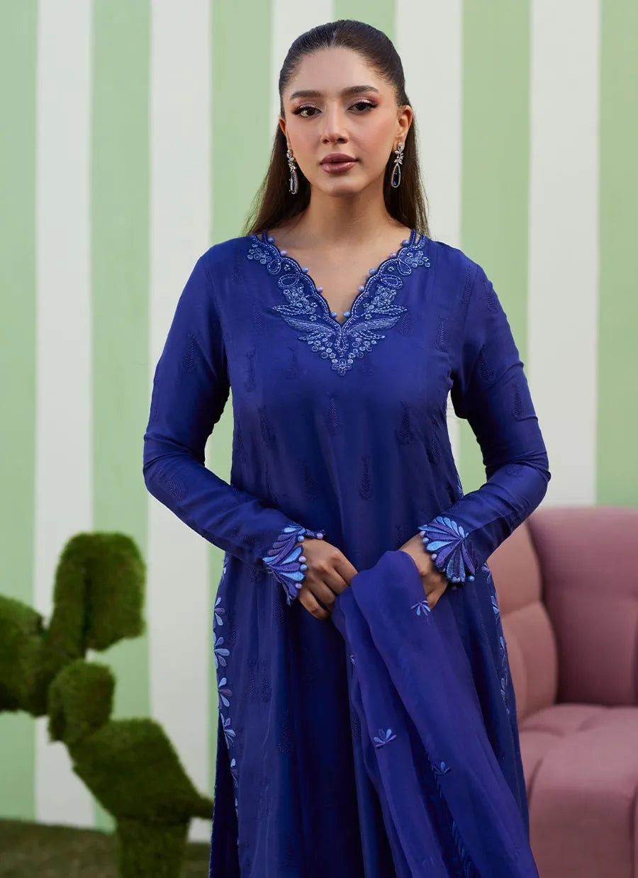 Woman wearing a blue embroidered dress against a green and white striped wall.