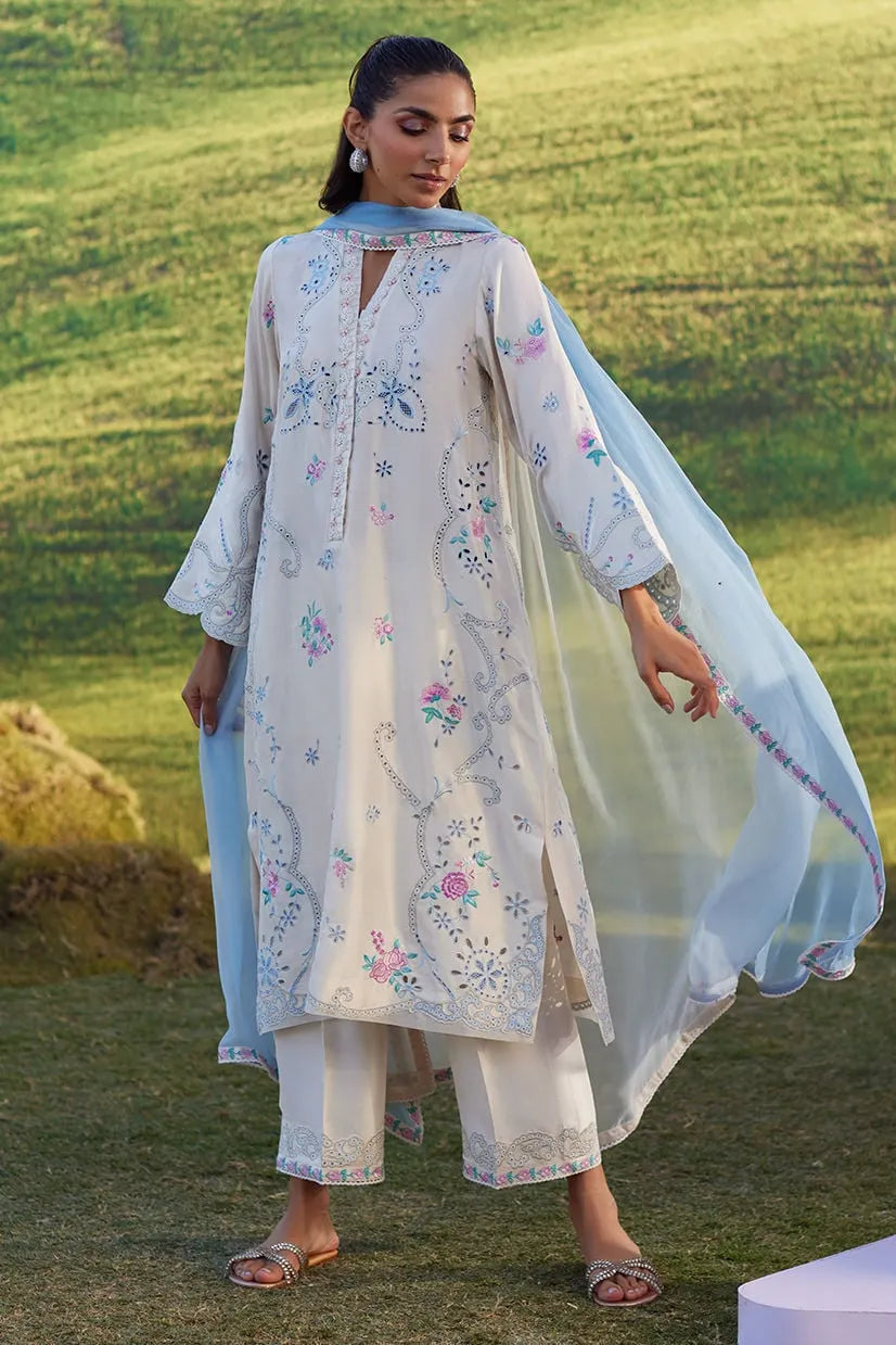 Woman in a light-colored embroidered outfit standing outdoors on grass
