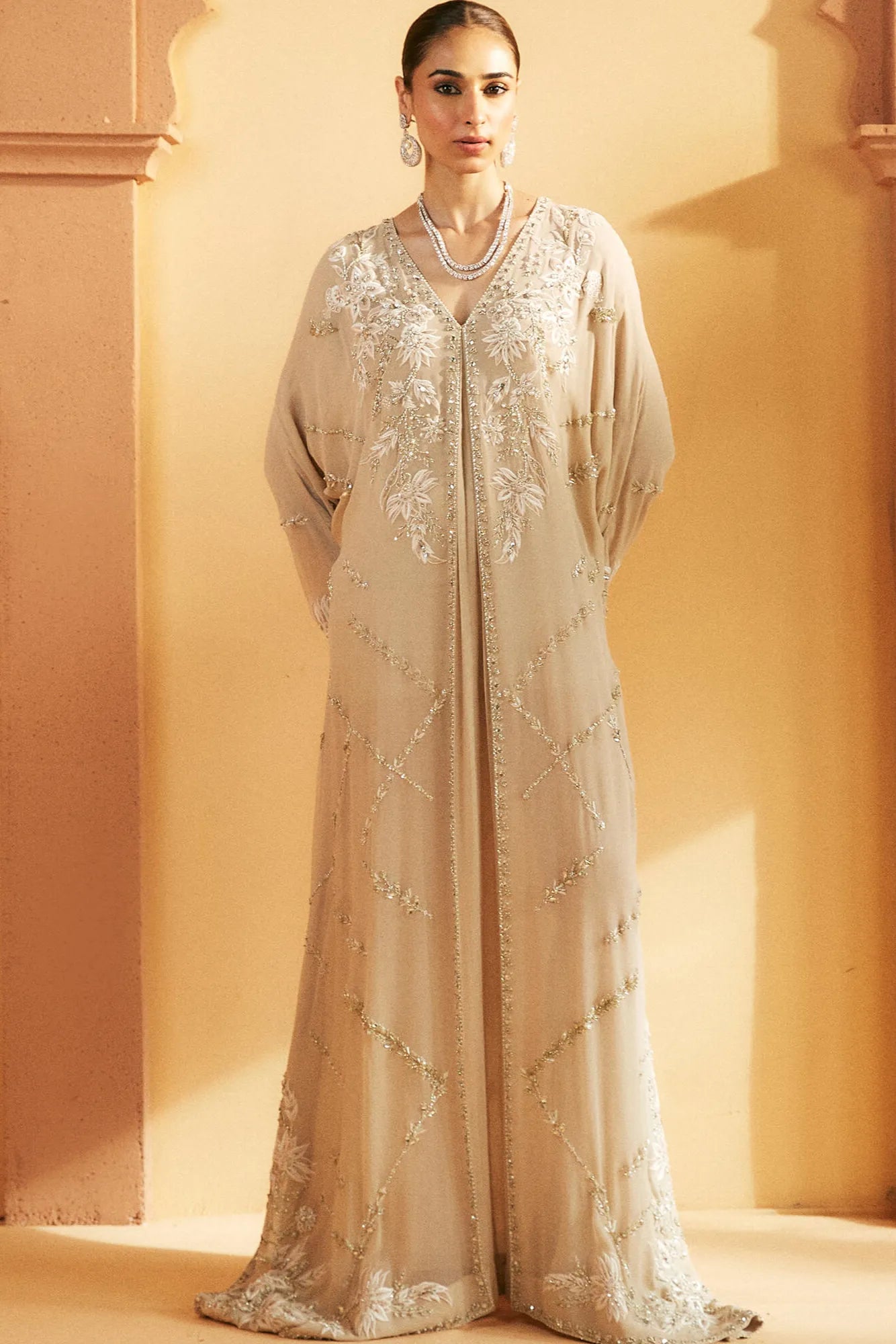Woman wearing a beige embroidered dress against a warm-toned wall.