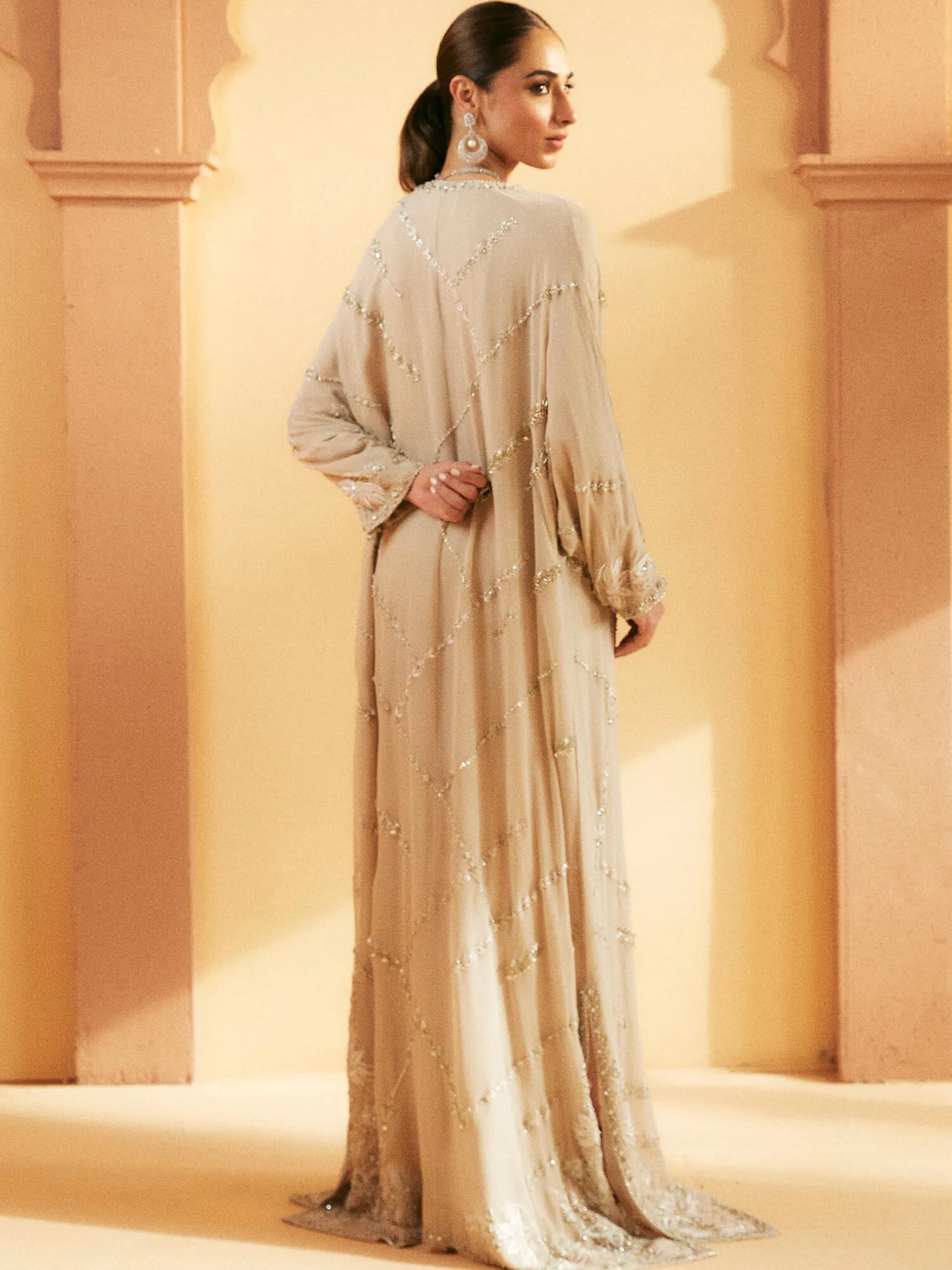 Woman in a long, light-colored dress standing against a warm-toned wall.
