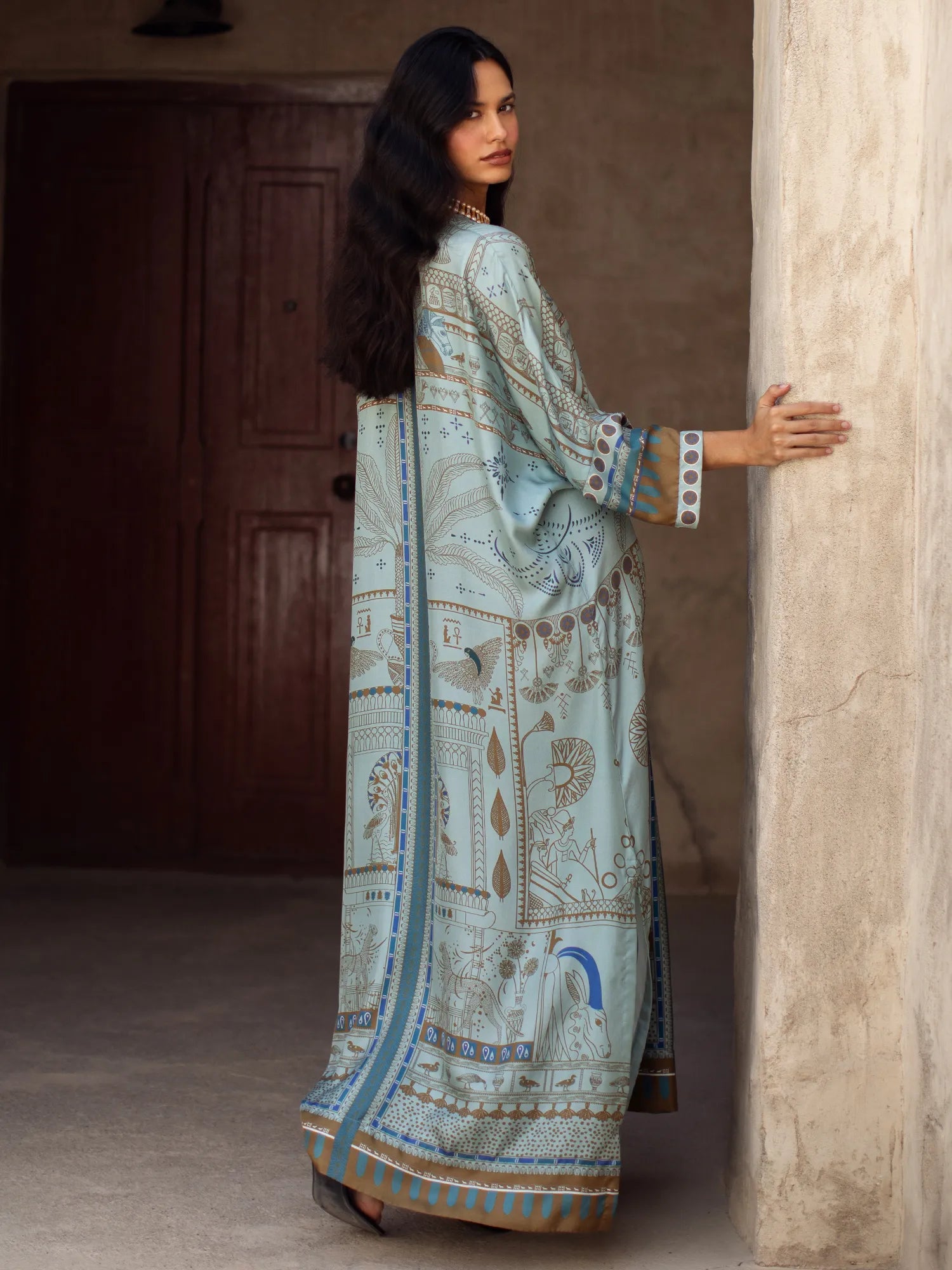 Woman in a light blue embroidered traditional outfit standing against a stone wall.