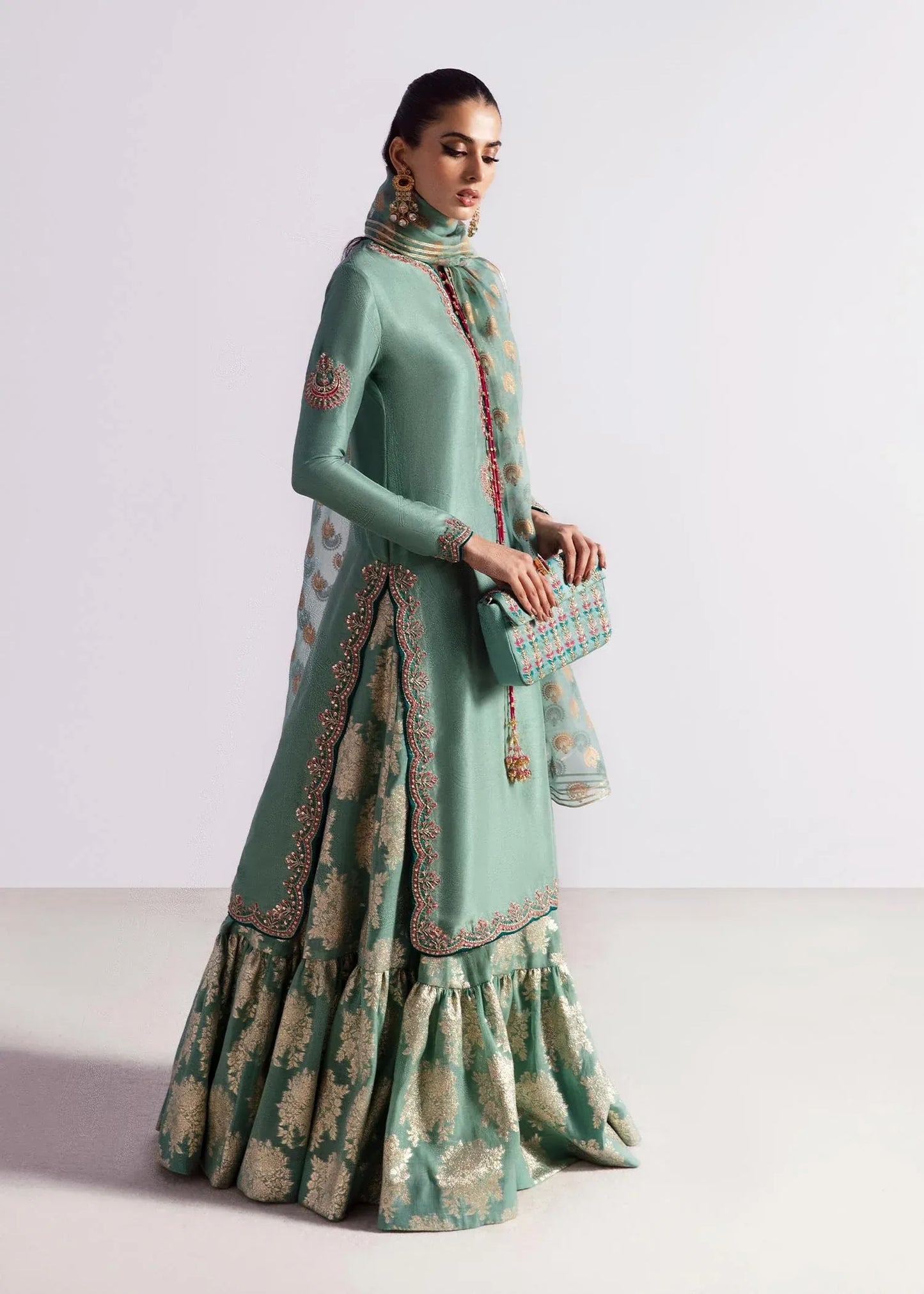 Woman wearing a traditional green and beige outfit with intricate patterns on a white background