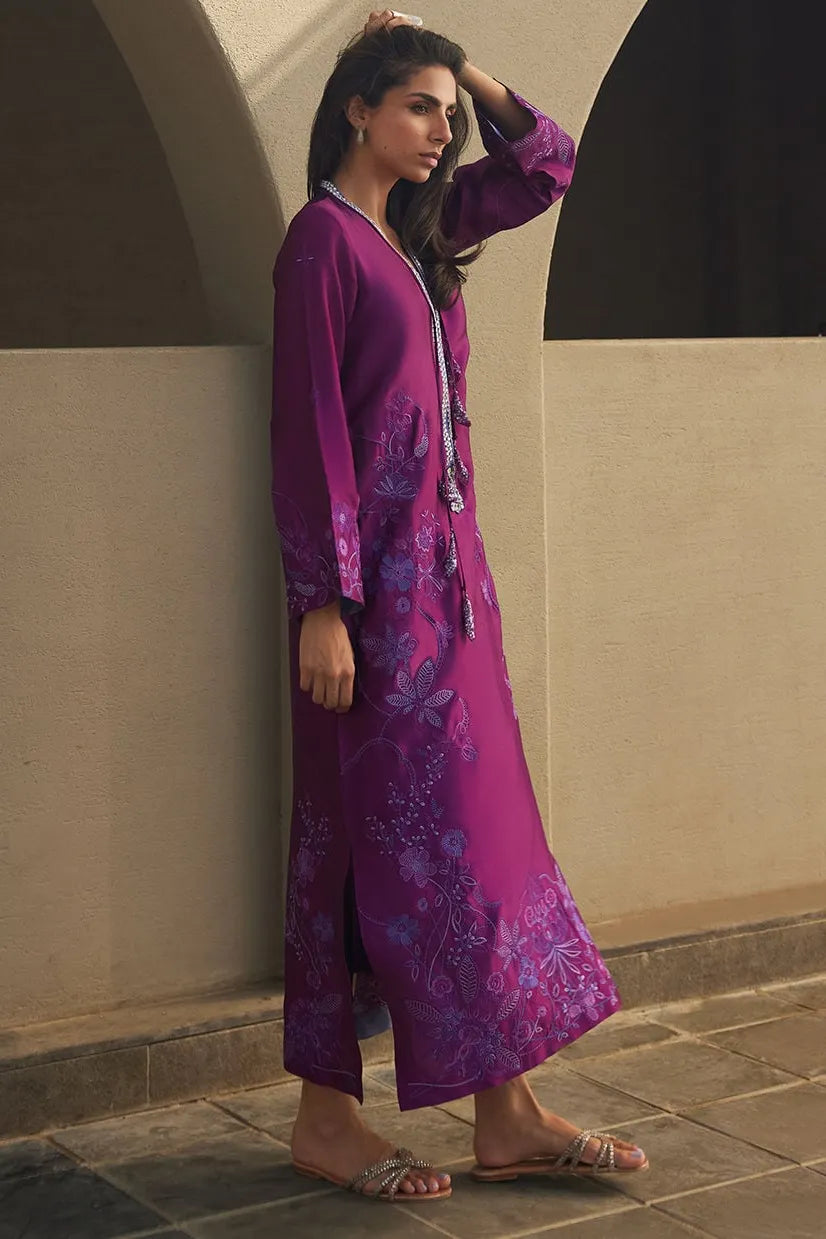 Woman in a purple floral dress standing against a beige wall.