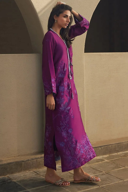 Woman in a purple floral dress standing against a beige wall.