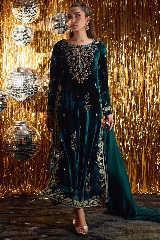 Woman in a dark green embroidered dress standing against a gold glittery curtain with disco balls.