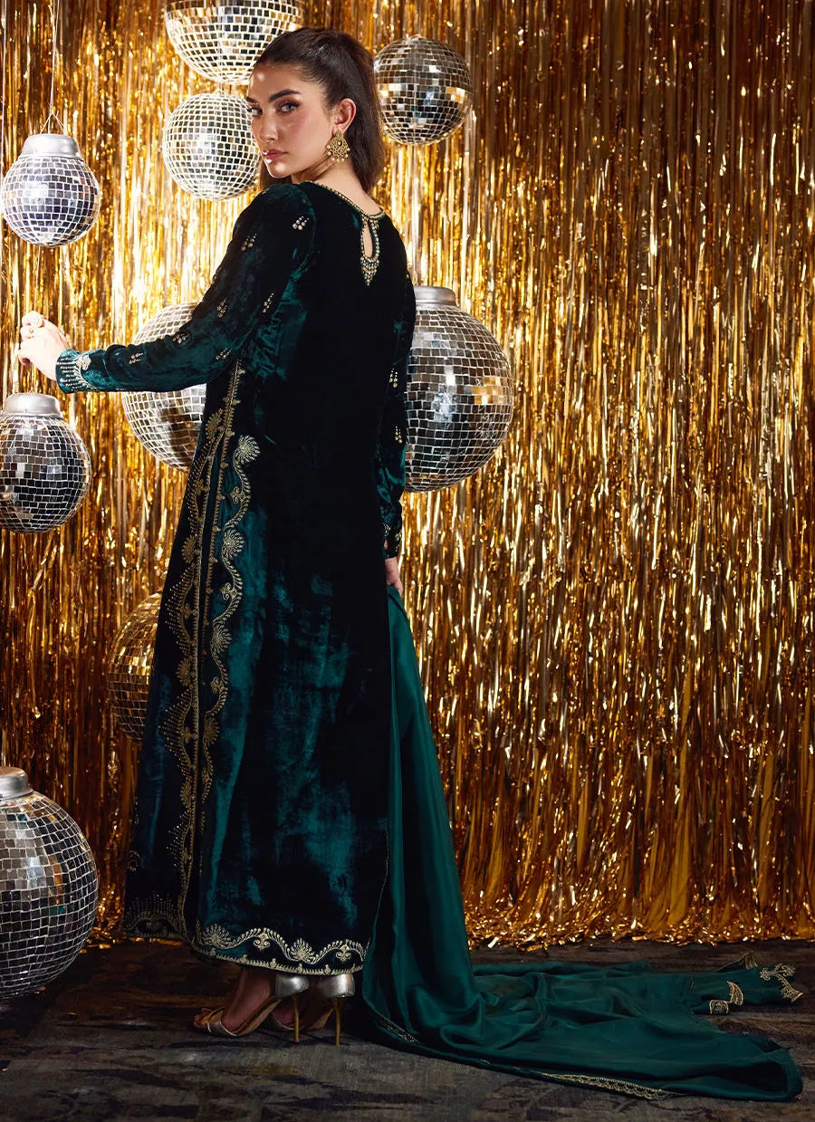 Woman in a green dress with gold embroidery standing in front of a gold curtain with disco balls.