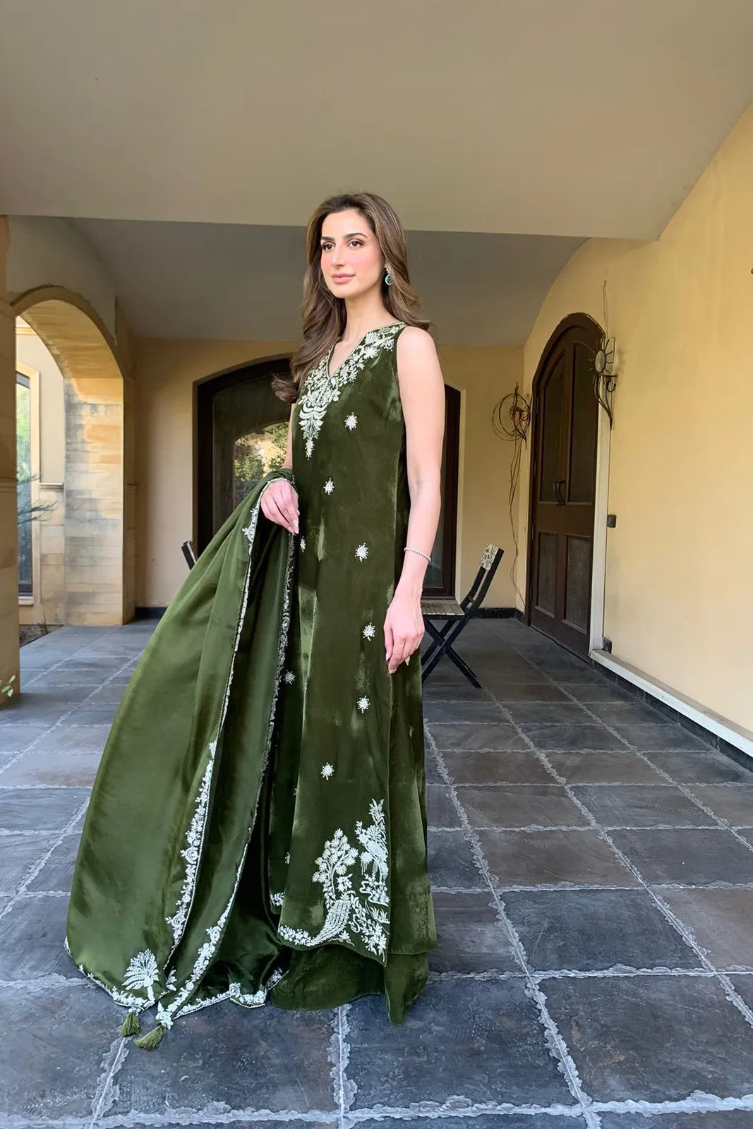 Woman in a green dress with white embroidery standing in an outdoor setting.