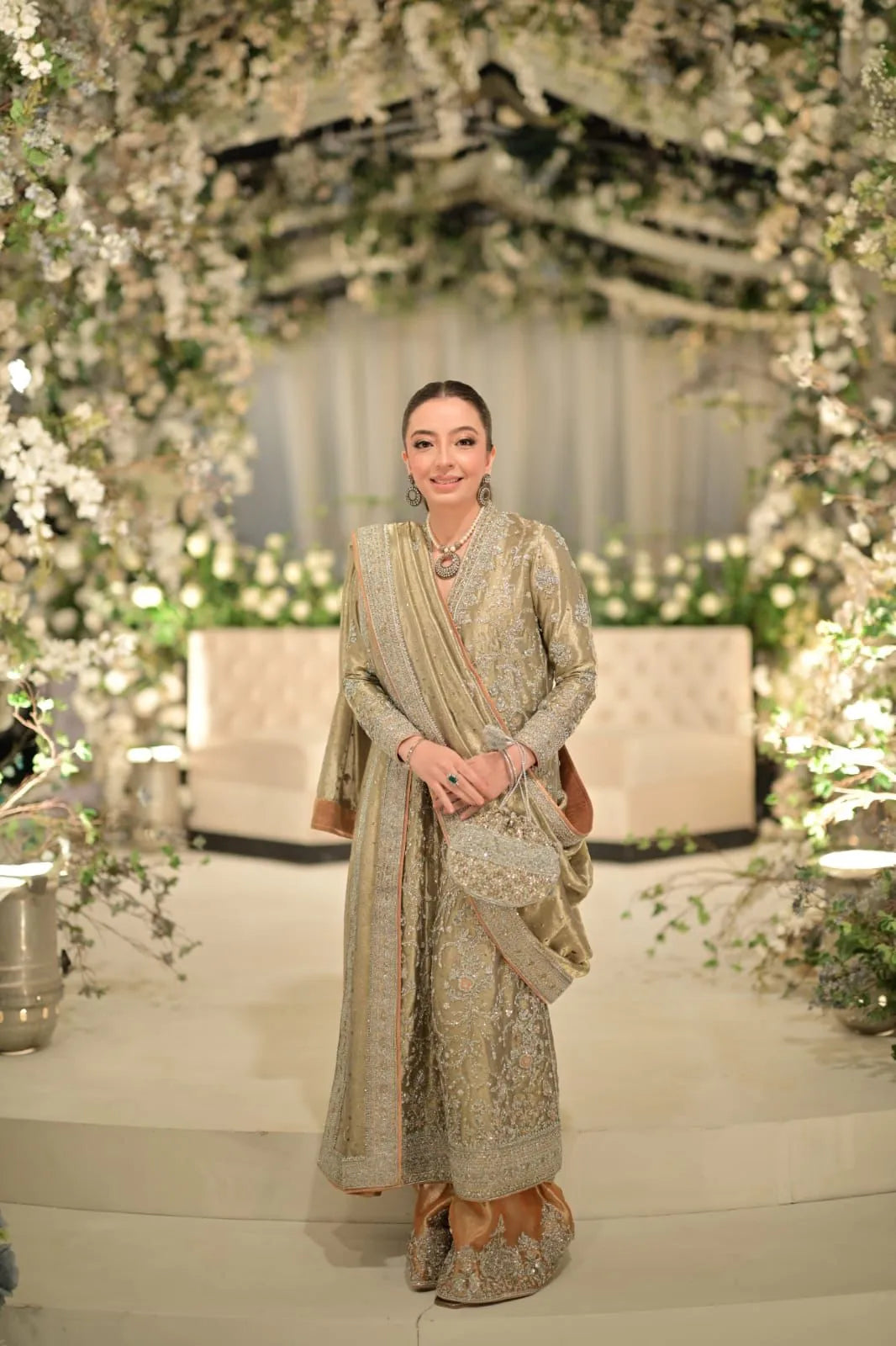 Woman in traditional attire standing in a decorated indoor setting with floral arrangements.