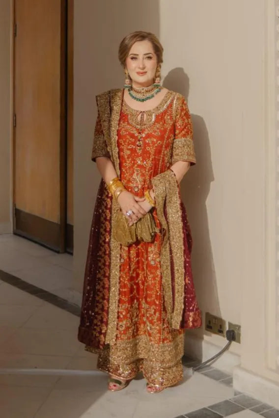 Woman in traditional red and gold outfit standing indoors.