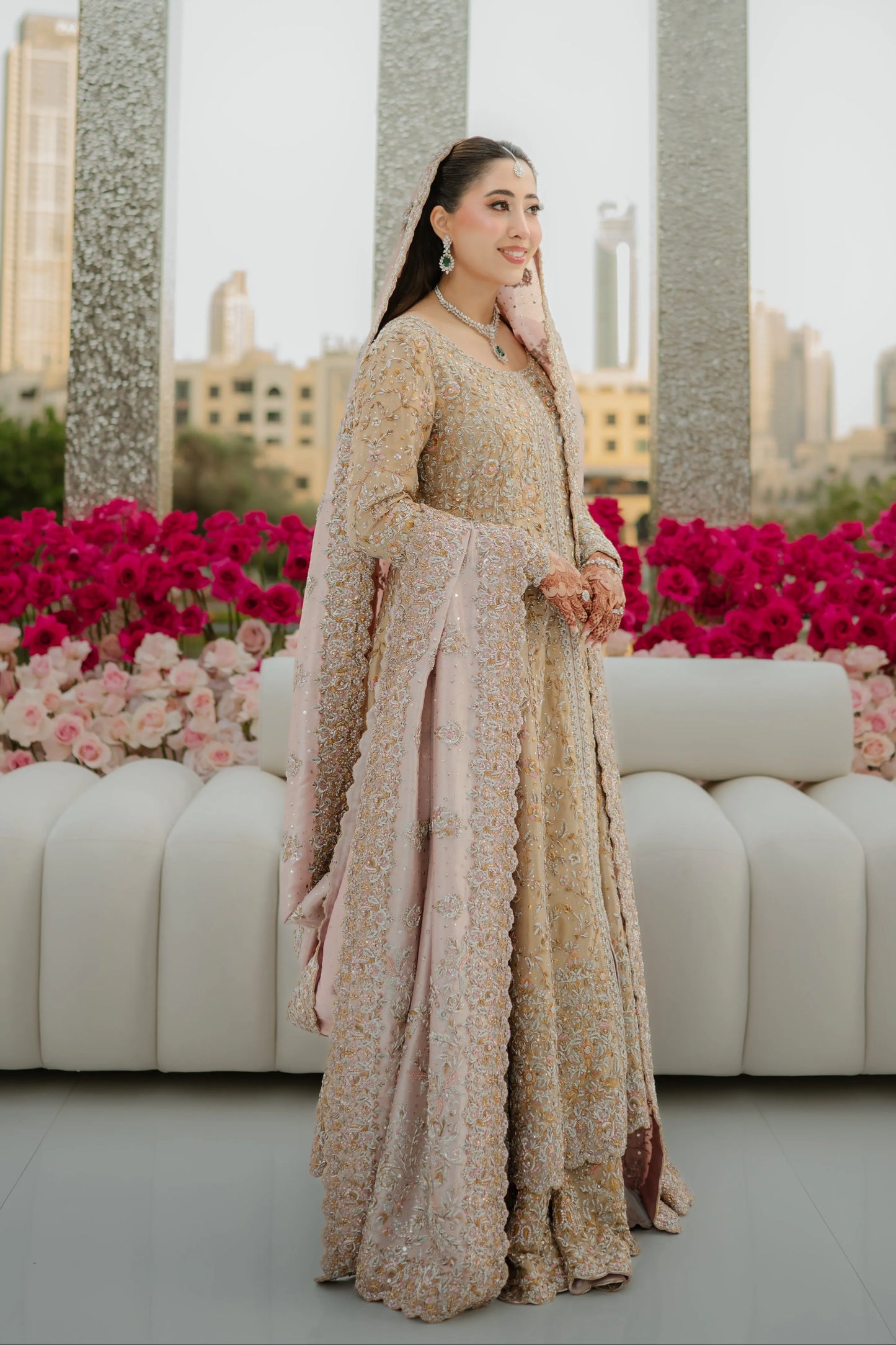 Woman in a floral dress standing in front of pink flowers and a cityscape.