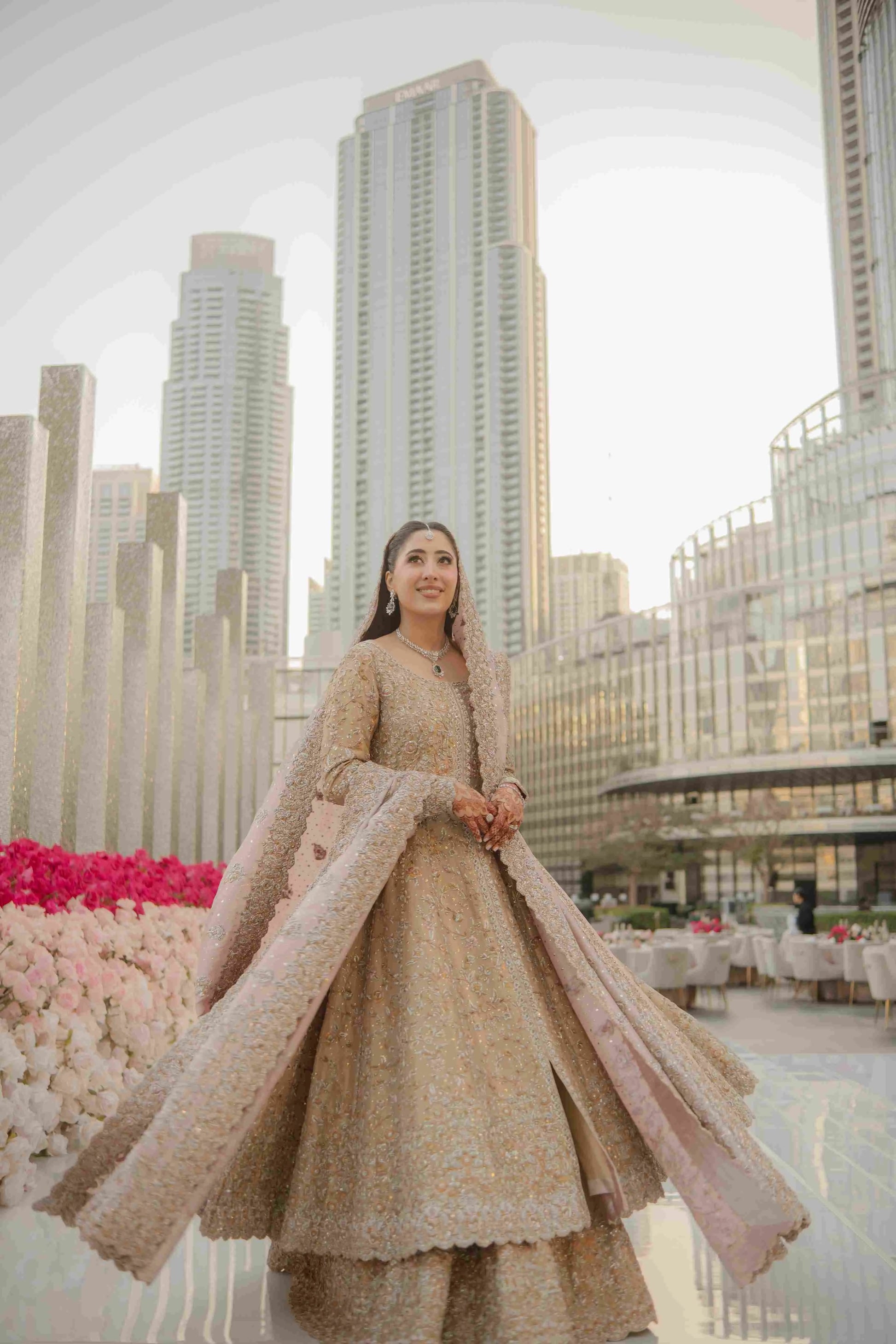 Woman in traditional outfit standing in front of modern cityscape with tall buildings.