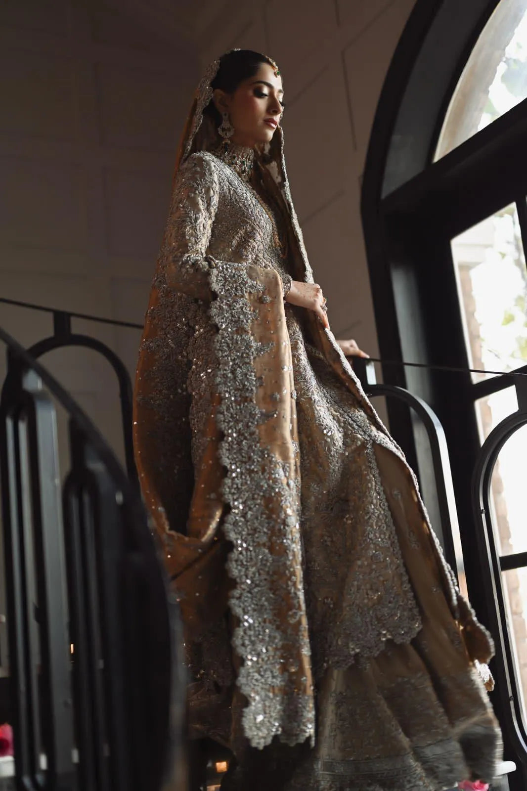 Woman in a traditional outfit with intricate designs standing indoors.