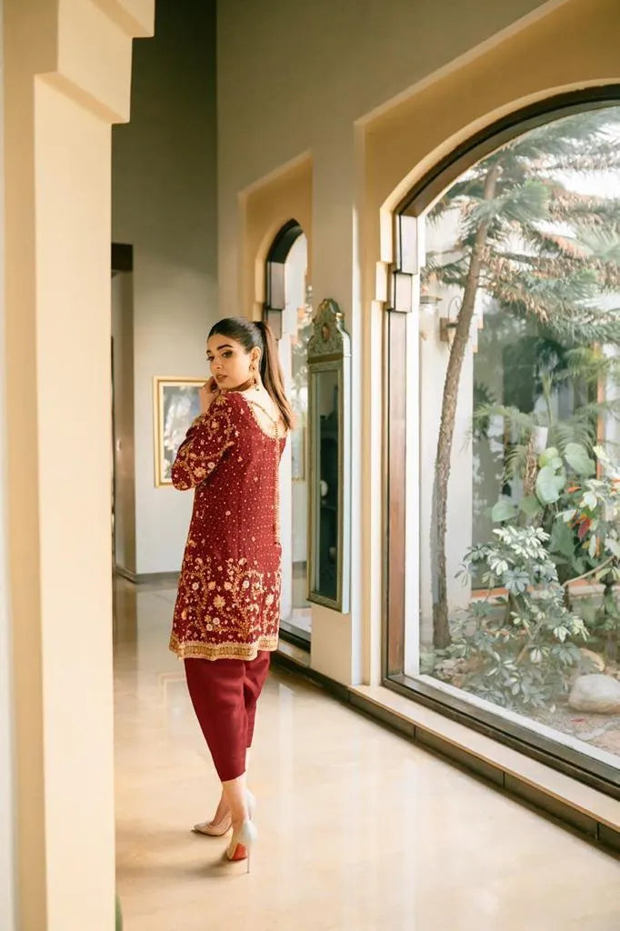 Woman in a red traditional outfit standing in a room with large windows.