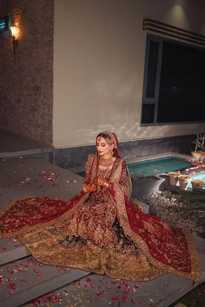 Woman in a traditional red and gold outfit sitting by a pool with flower petals.