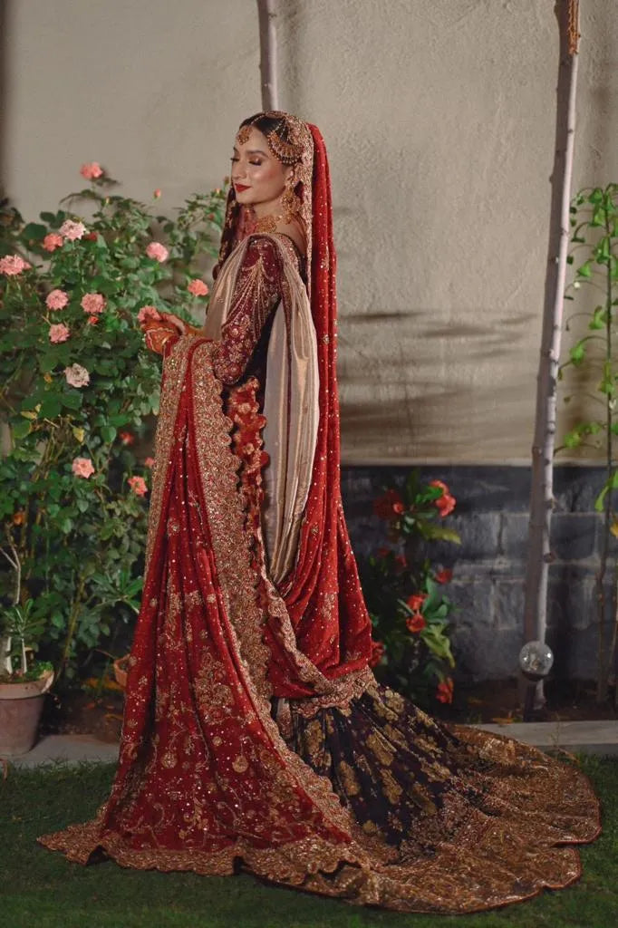 Woman in a traditional red and gold embroidered outfit standing outdoors with plants in the background