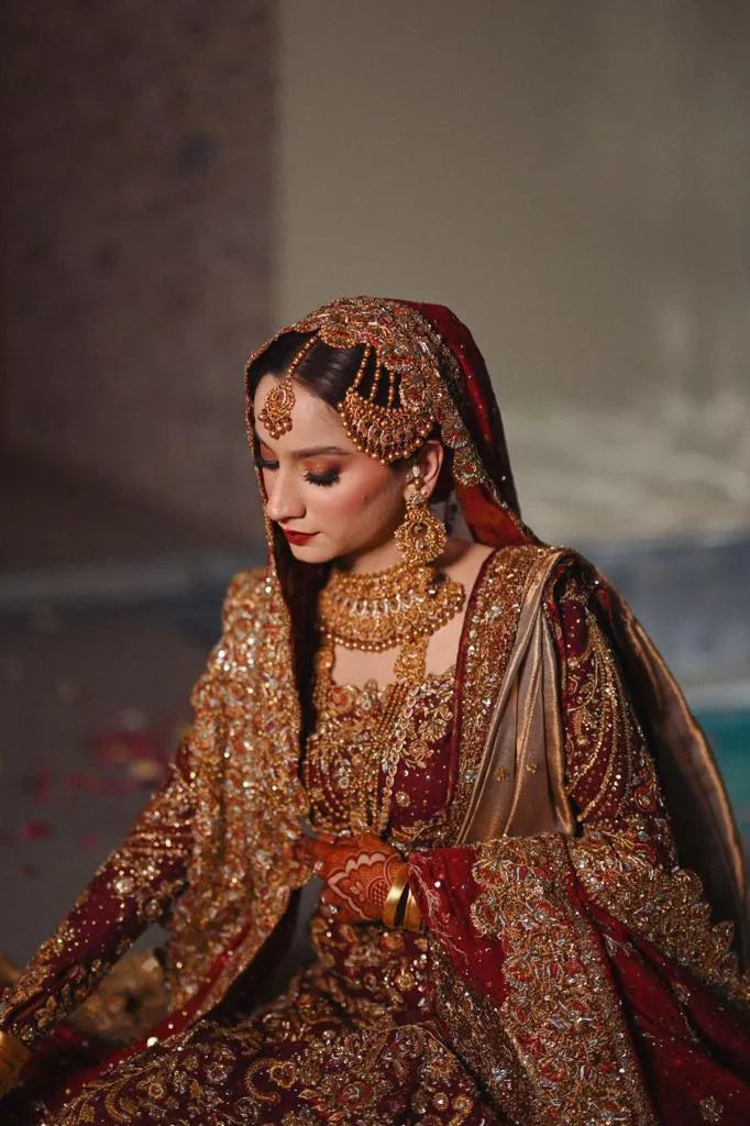 Woman in traditional embroidered outfit with jewelry, sitting indoors.