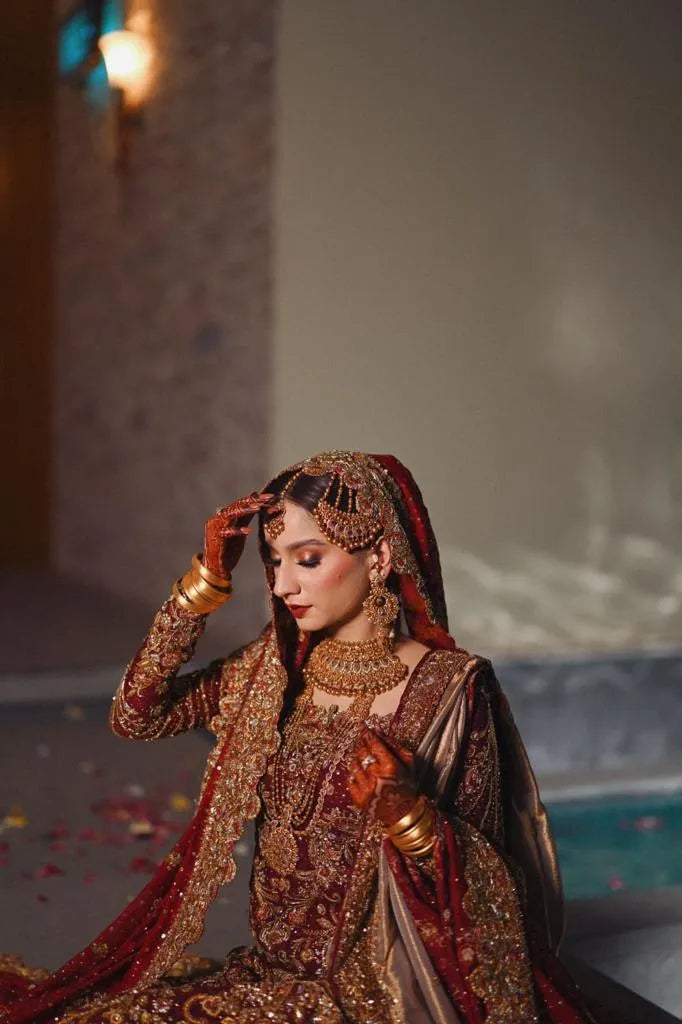 Woman in traditional embroidered outfit with jewelry, sitting indoors.