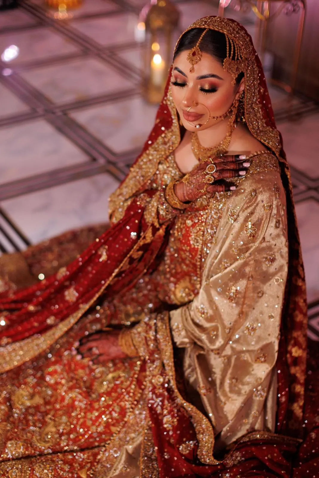 Woman in traditional gold and red bridal outfit with intricate jewelry.