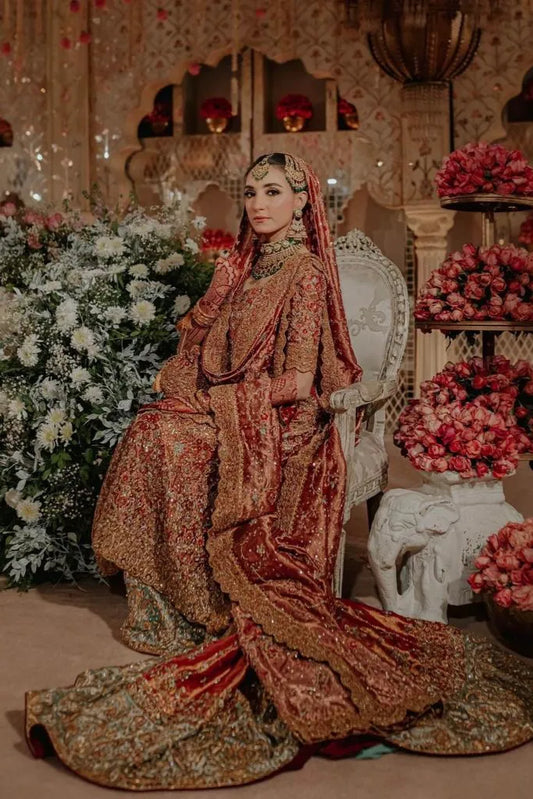 Woman in traditional attire sitting in a decorated room with flowers and furniture.