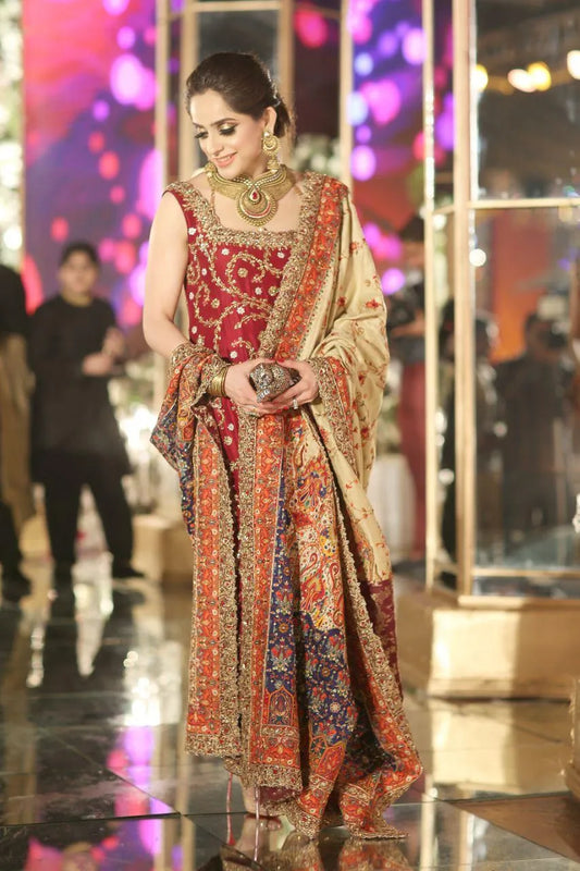 Woman in a traditional red and gold outfit with a patterned shawl, standing in a reflective surface setting.