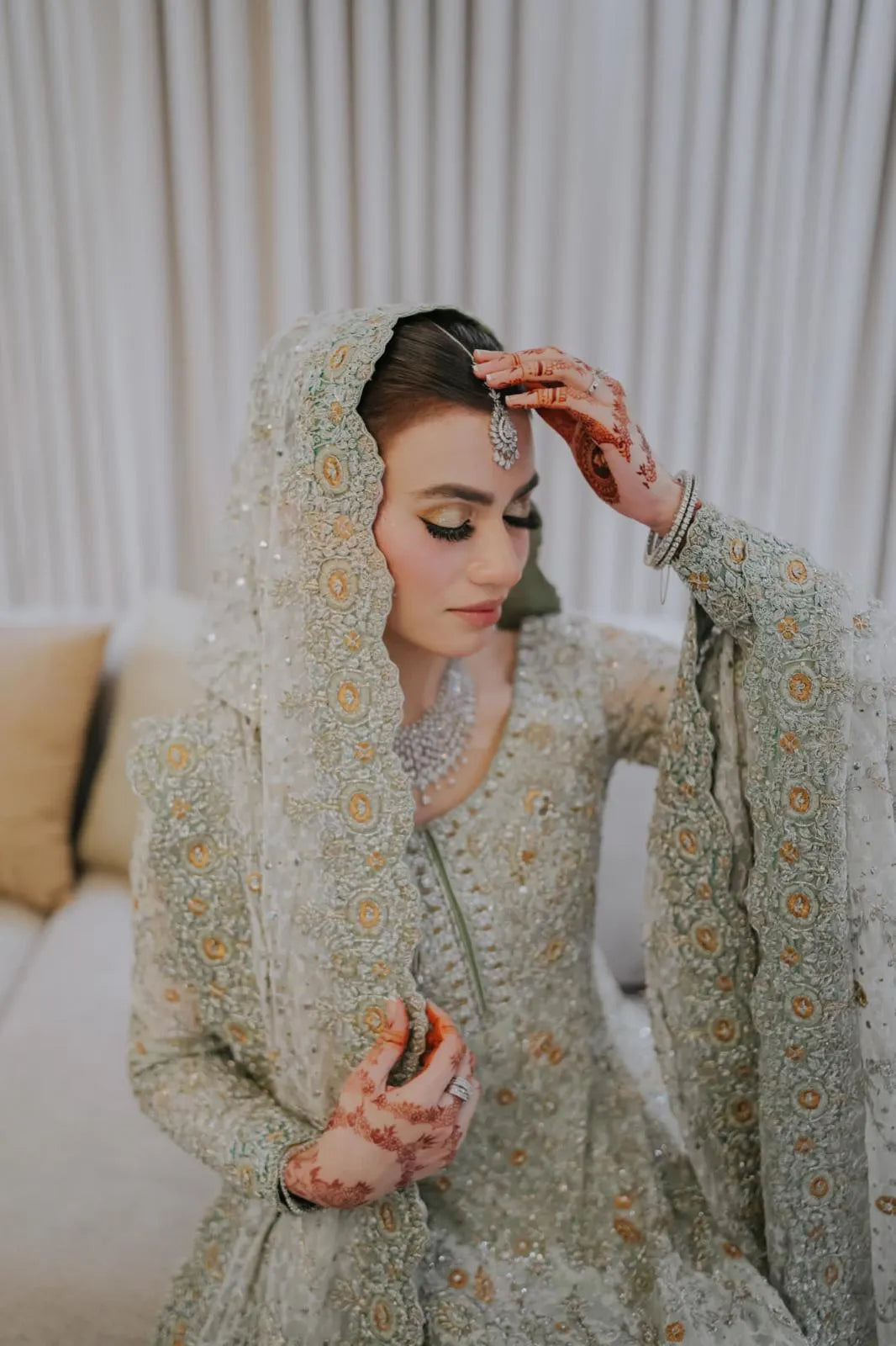 Woman in traditional embroidered outfit adjusting her headscarf indoors.