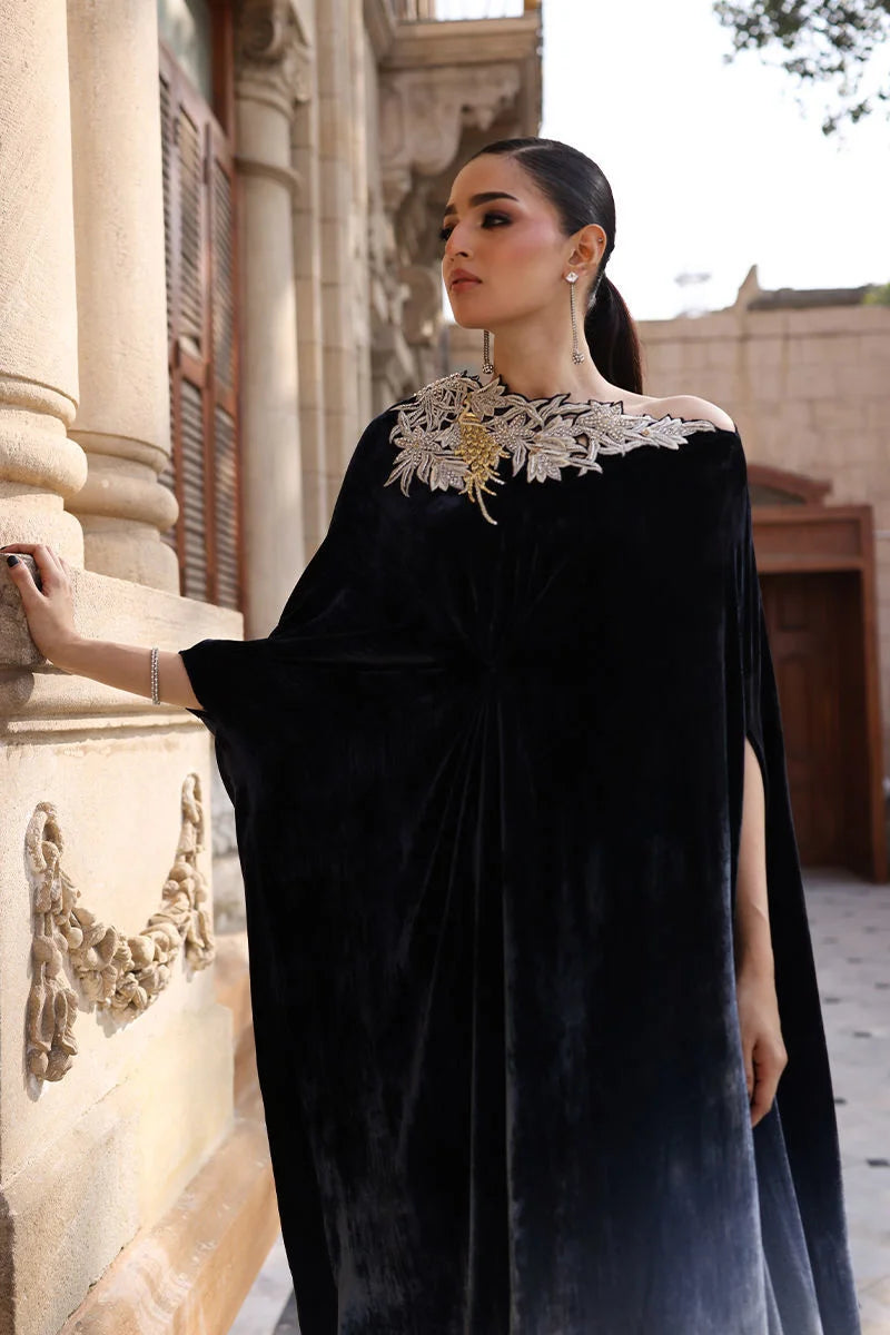 Woman in a black velvet dress with lace details standing outdoors.