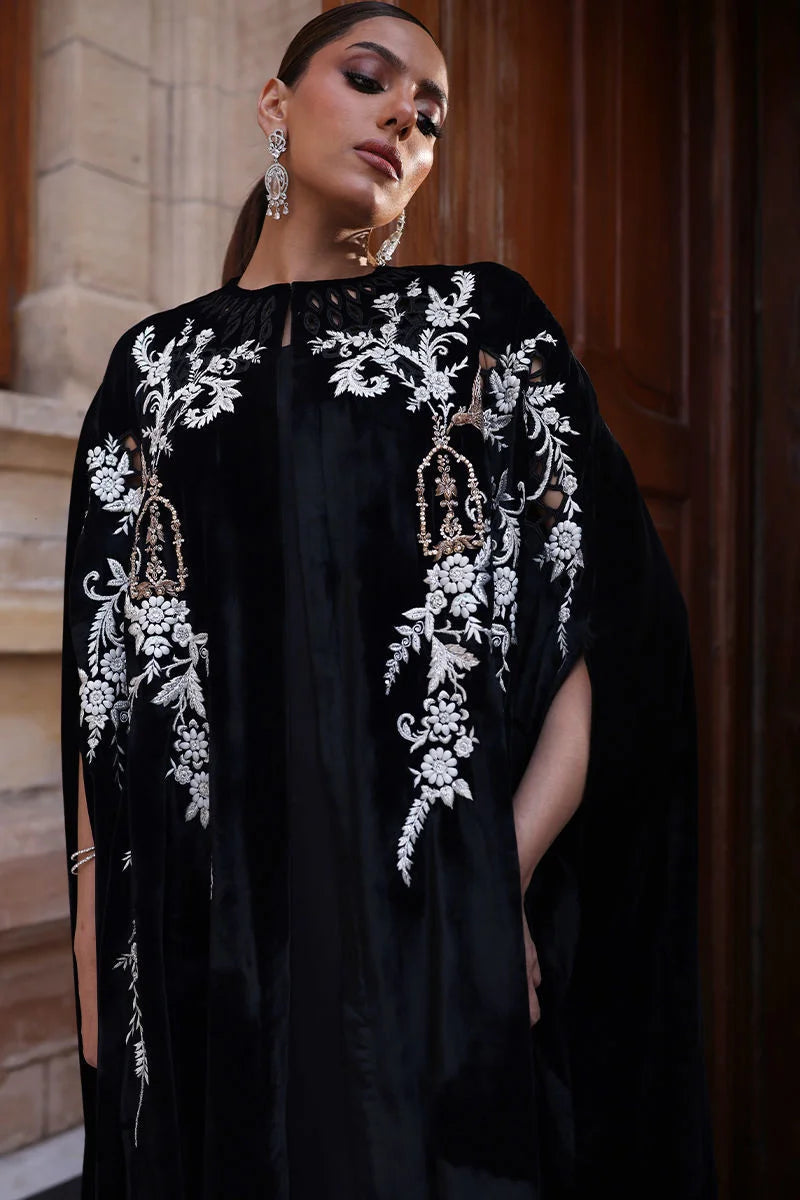 Woman wearing a black dress with white floral embroidery in an indoor setting.