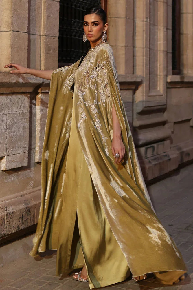 Woman in a gold saree with intricate designs standing against a stone wall.