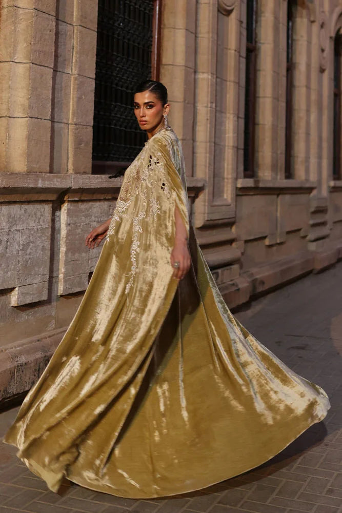 Woman in a gold saree standing in front of a stone building.