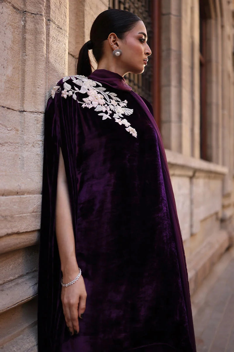 Woman wearing a purple velvet cape with white lace details against a stone building.