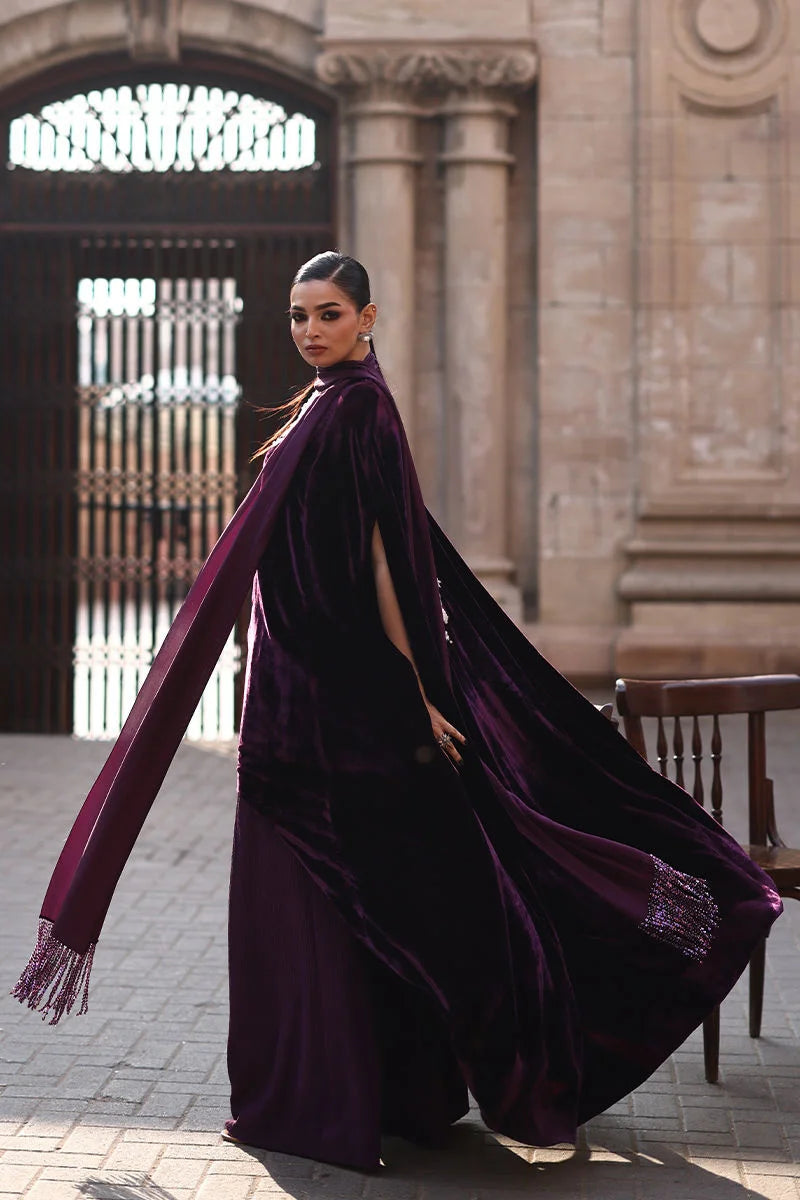 Woman in a long, dark purple dress with a cape walking outdoors.