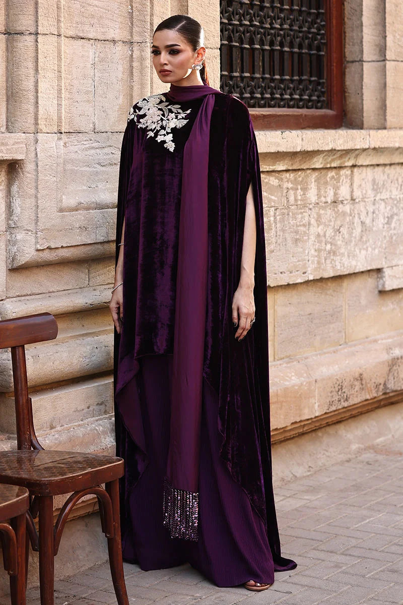 Woman in a long, dark purple dress with white embroidery standing in front of a stone wall.