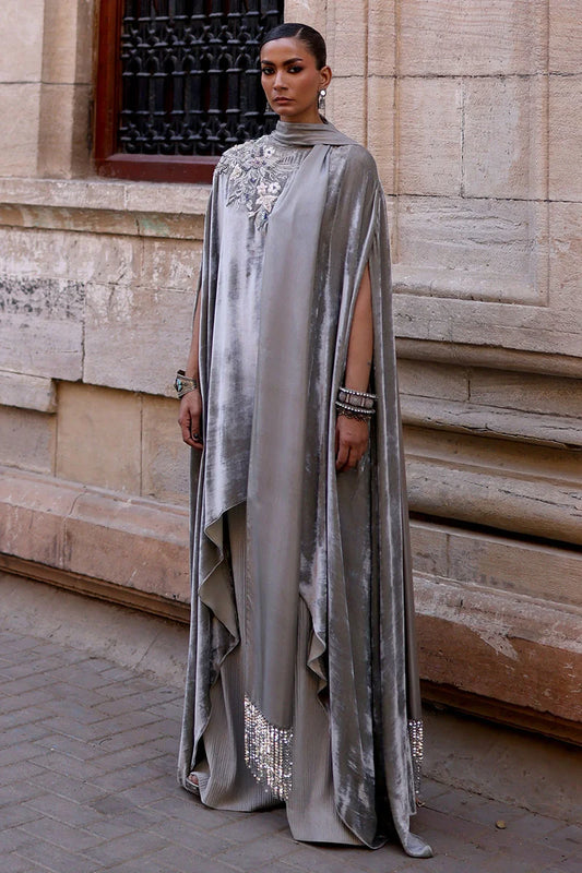 Woman wearing a long, elegant silver dress with intricate detailing against a stone wall.