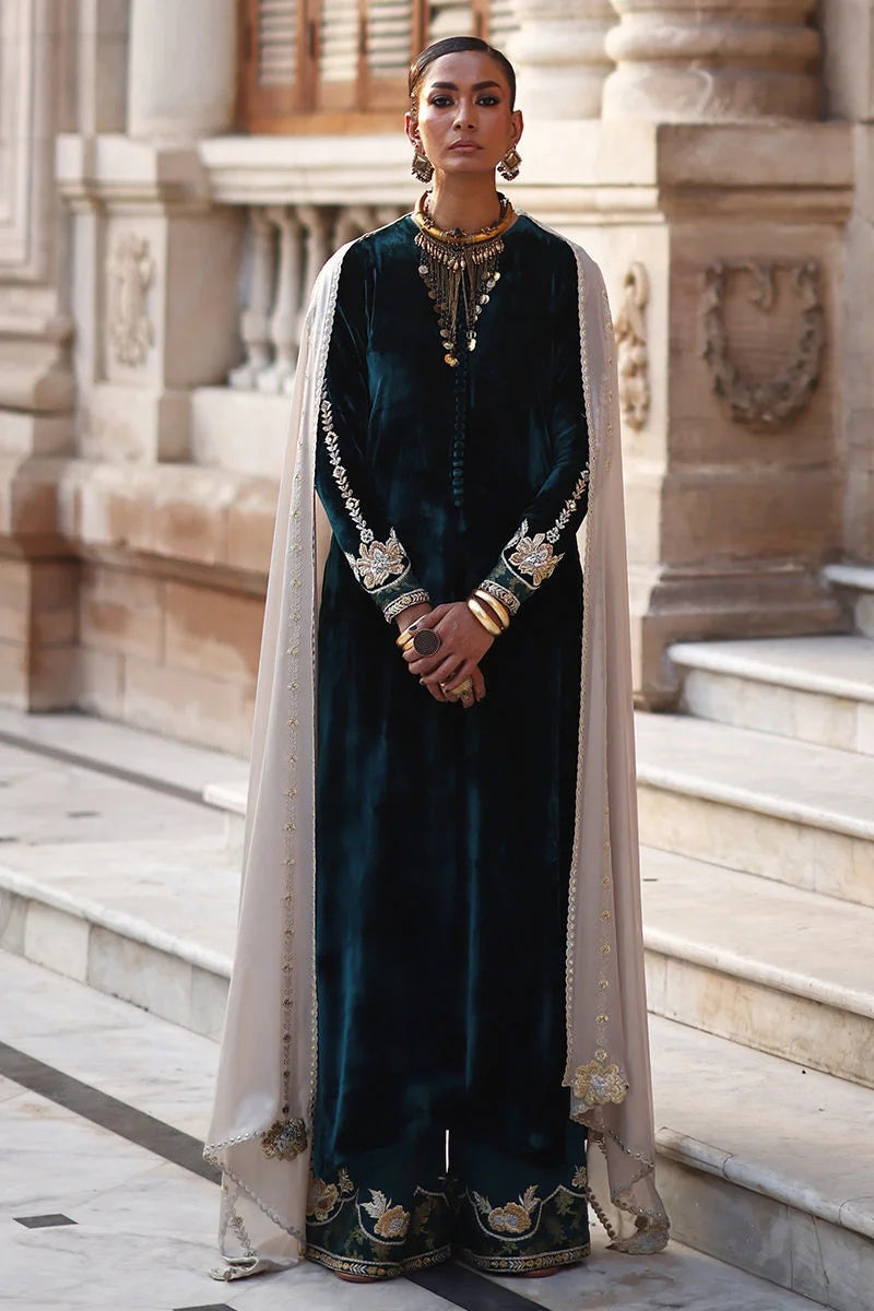 Woman in traditional dark green velvet outfit with gold embroidery standing in front of a classical building.