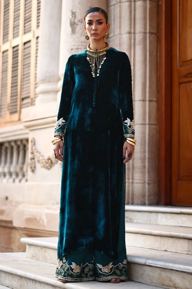 Woman in a long, dark green velvet dress with floral embroidery standing on steps.