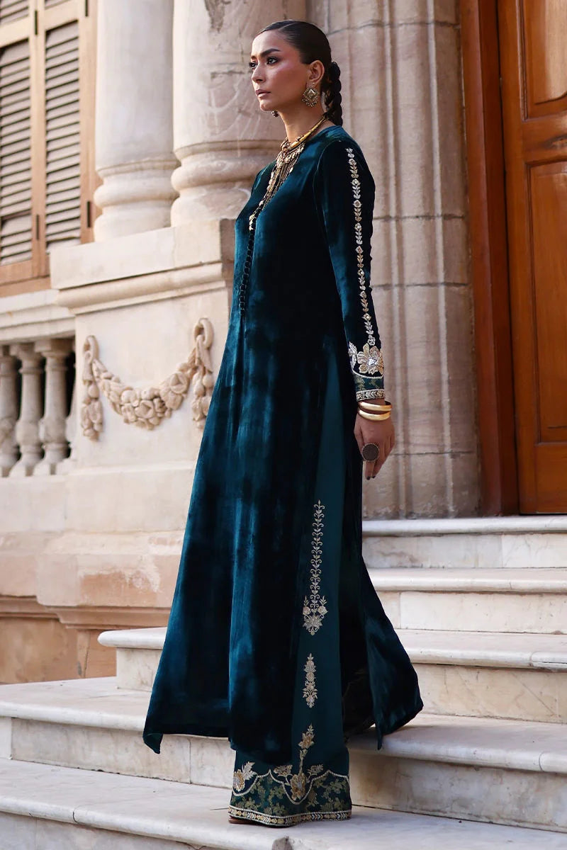 Woman in a dark green embroidered dress standing on steps of an elegant building.