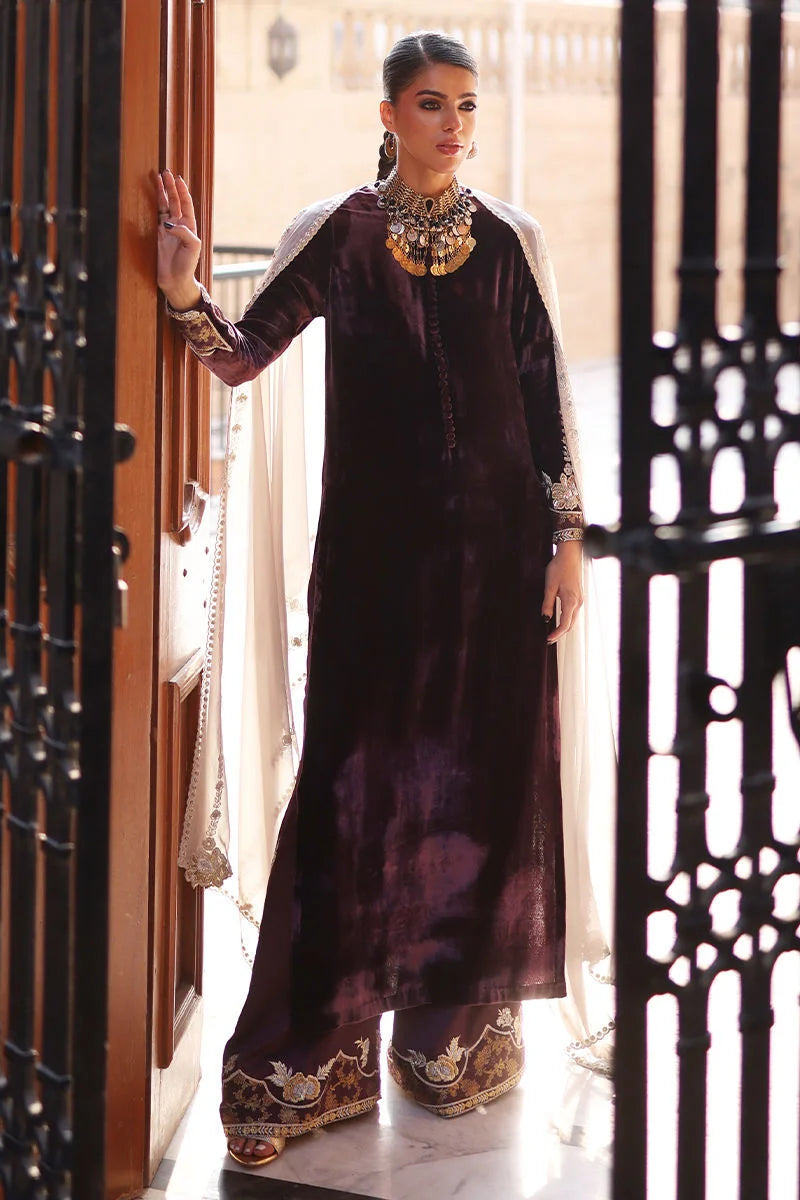 Woman in a long, dark purple dress with gold embroidery standing in a doorway.