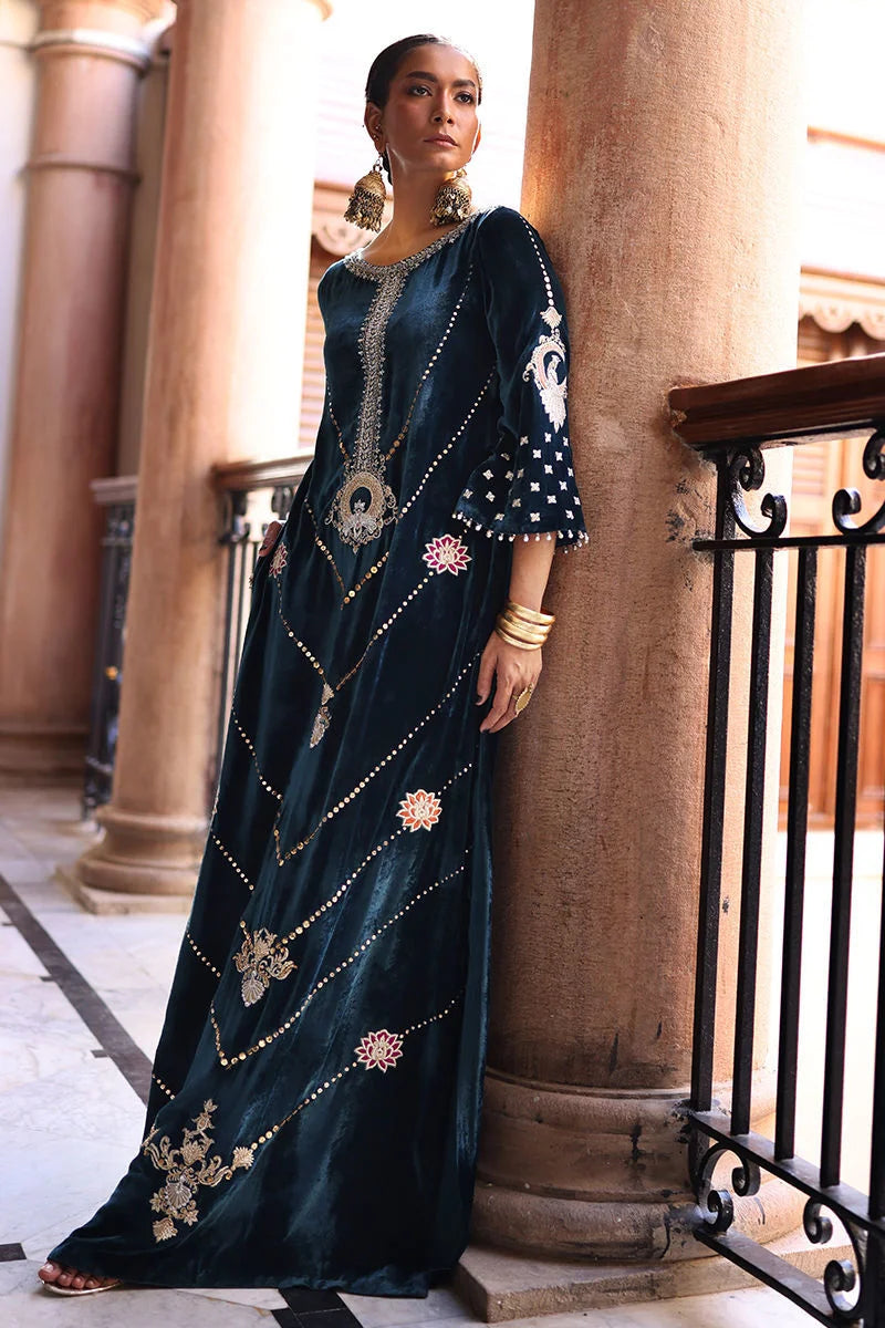 Woman in an ornate dark blue dress standing on a balcony with architectural columns in the background.