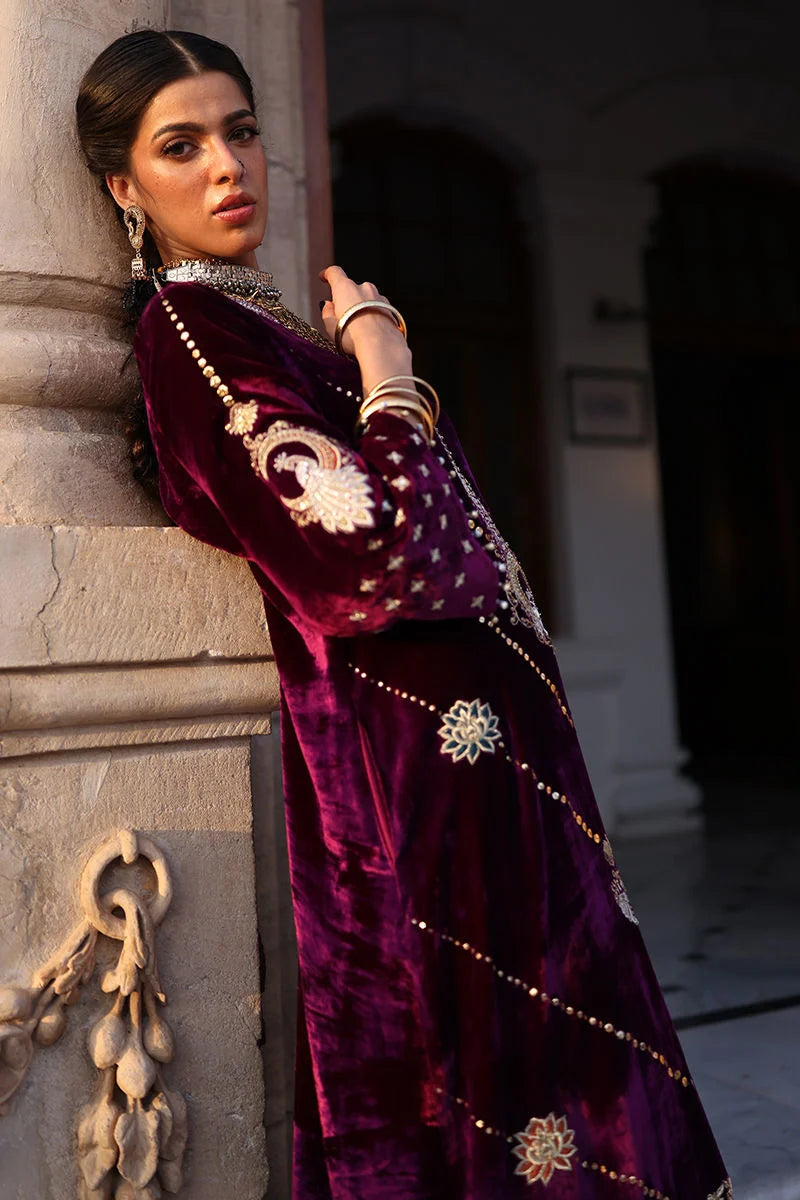 Woman in a traditional outfit with intricate designs leaning against a stone wall.