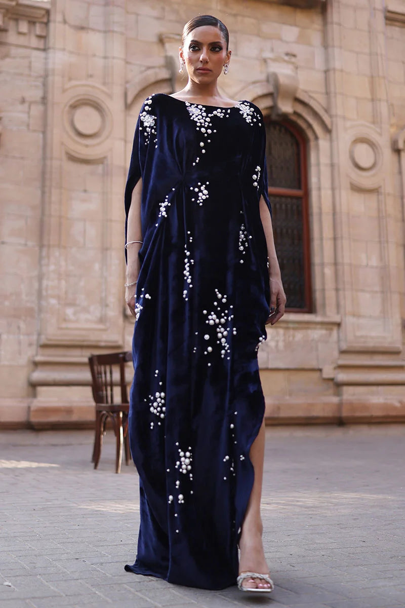 Woman wearing a dark blue evening gown with white floral embellishments in front of an architectural building.