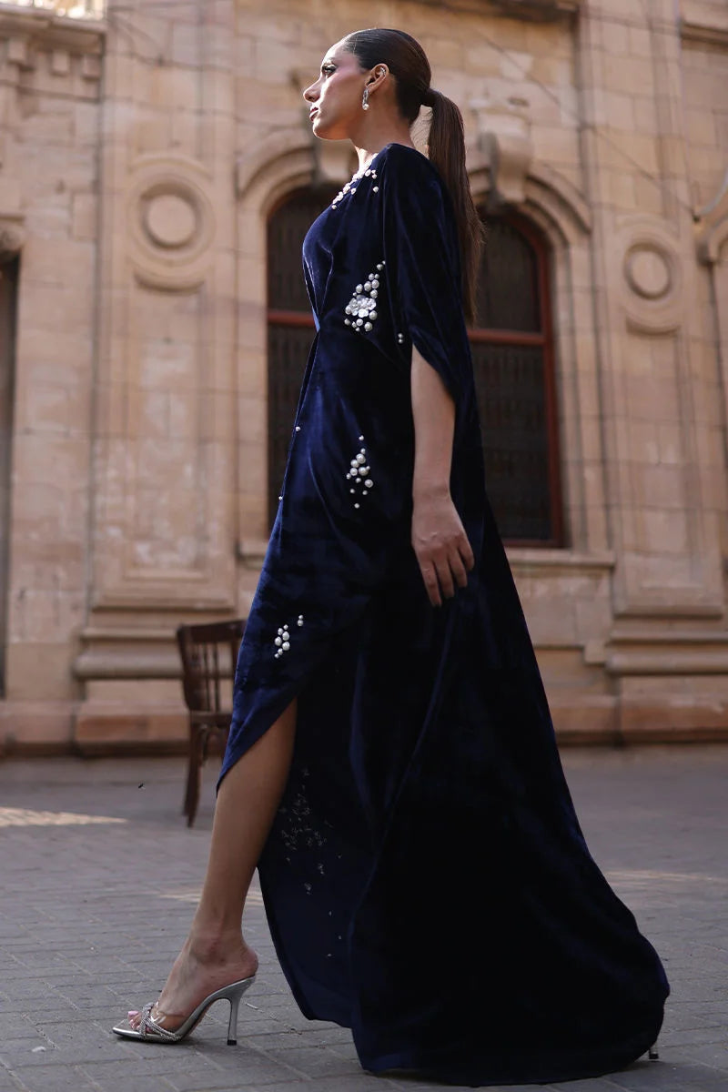 Woman in a dark blue dress with floral embellishments standing in front of a stone building.