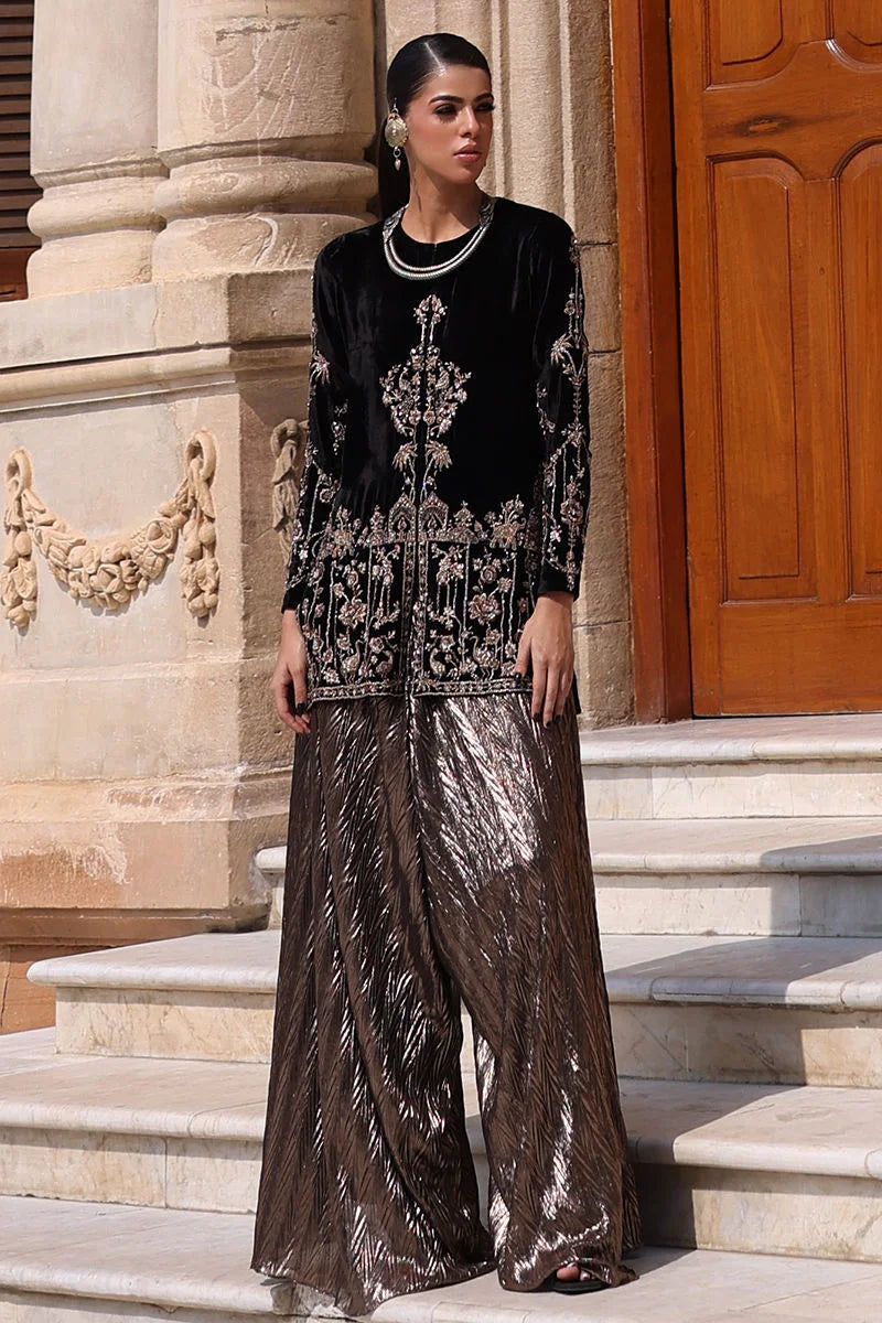 Woman in black embroidered top and brown patterned pants standing on stone steps.