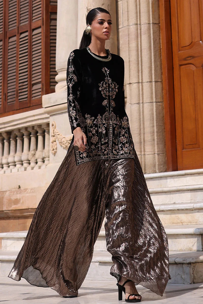 Woman in black and brown traditional outfit standing in front of a building.
