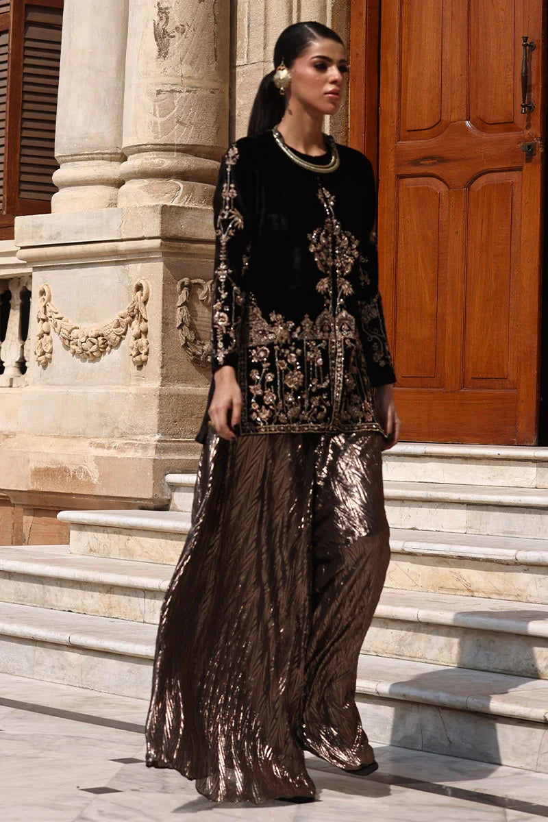 Woman in a black and gold outfit standing on steps in front of a building entrance.