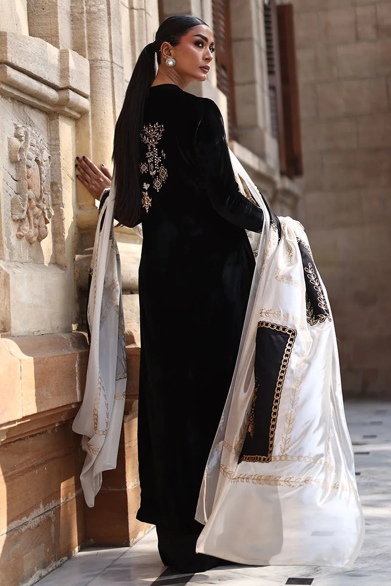 Woman in black and white traditional outfit with embroidery, standing against a stone wall.